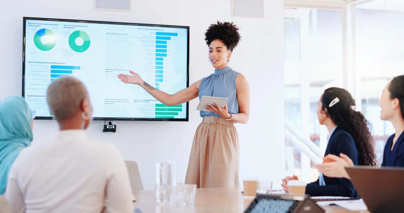 Business analyst presenting charts and data insights on a screen to colleagues.